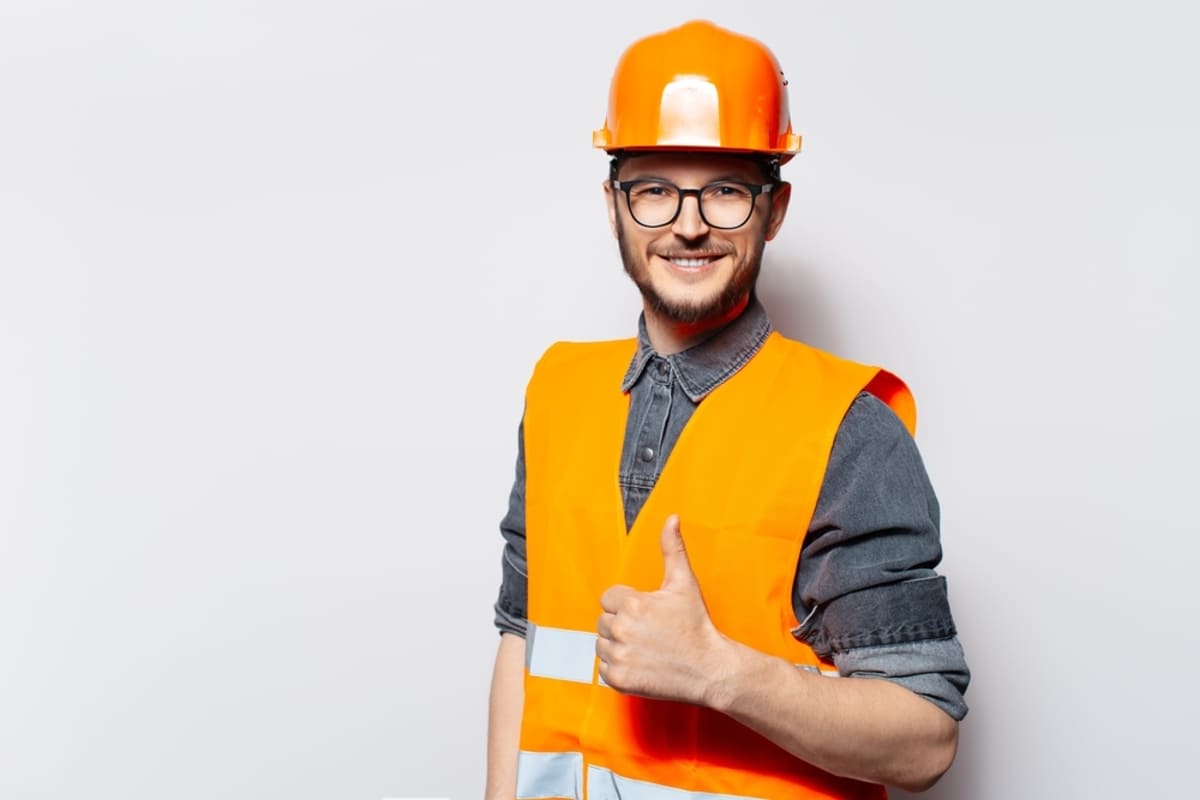 A man in an orange hard hat and vest giving a thumbs up