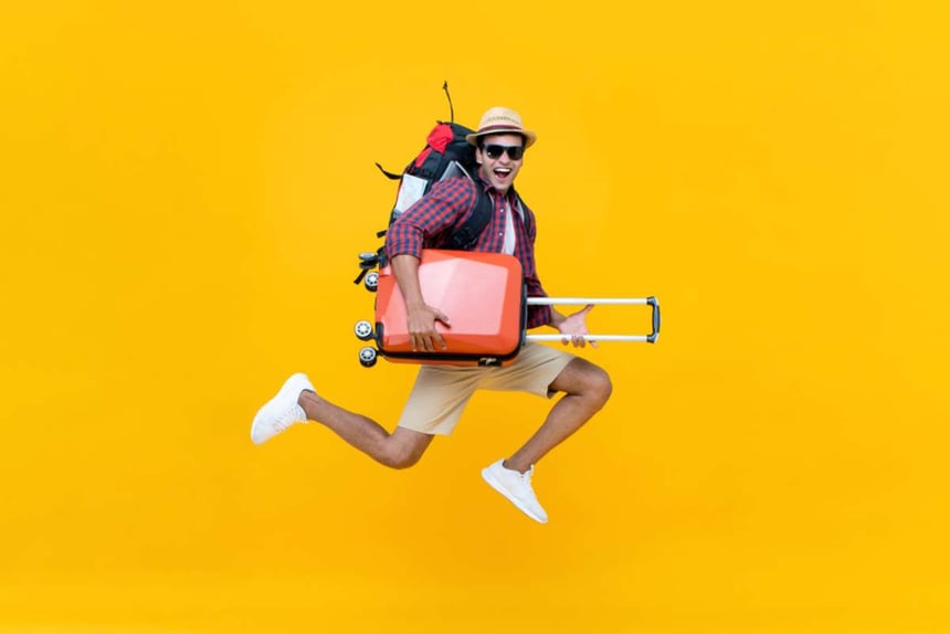 Excited happy young asian tourist with suitcases jumping isolated on yellow studio