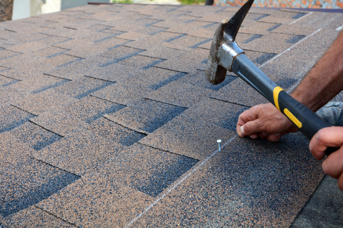 Someone hammering in asphalt shingles