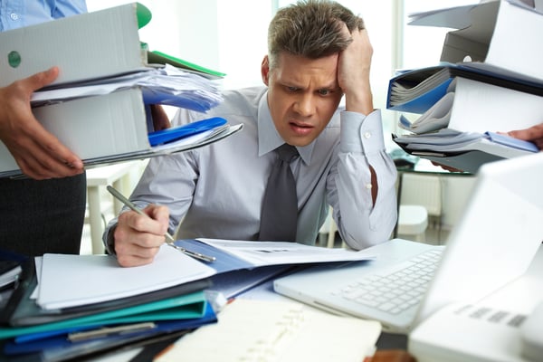 A man working on several binders of paperwork while others bring him more