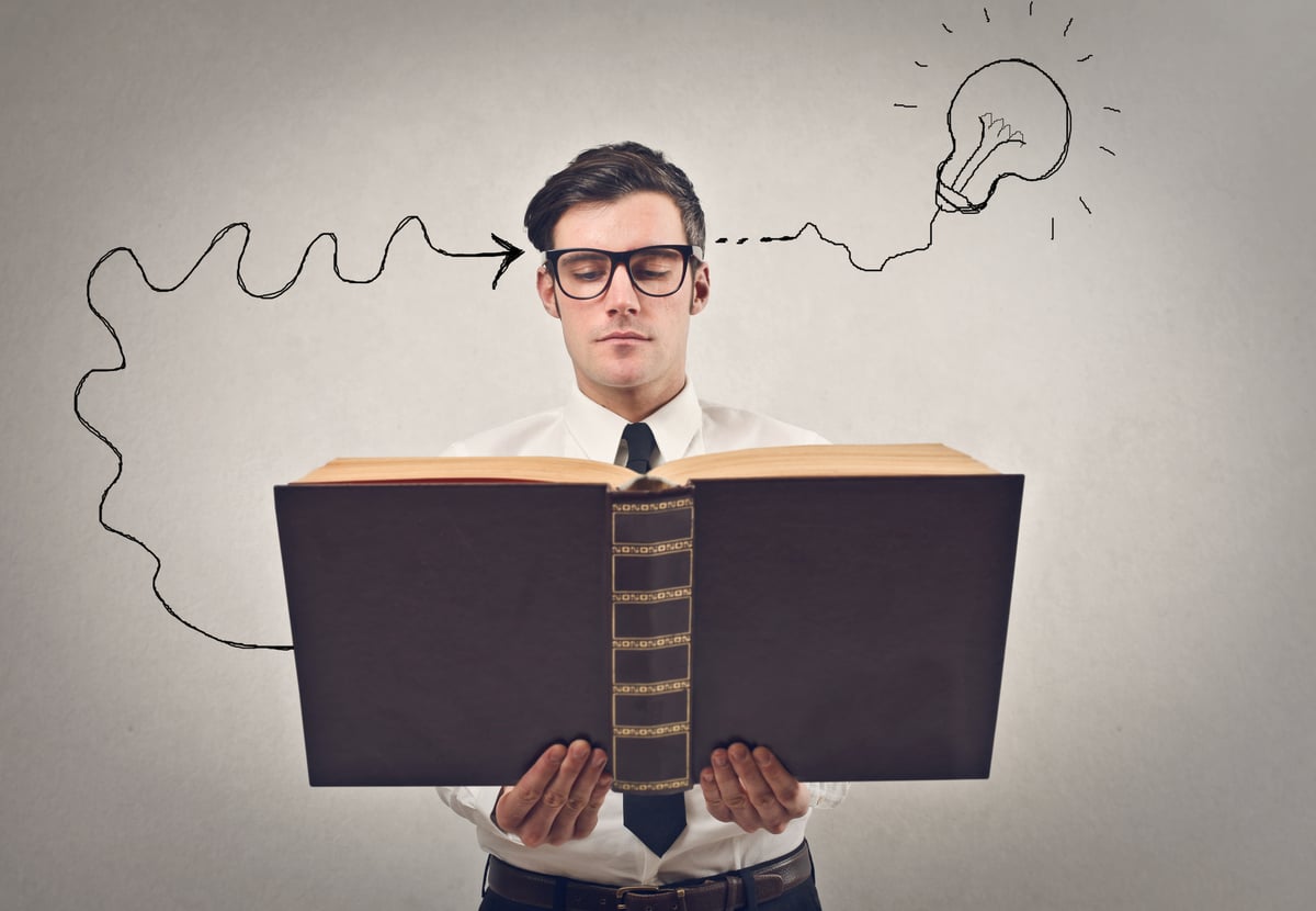 A man holding a book with a black arrow going from the book to his head and another black arrow from his head to a lightbulb