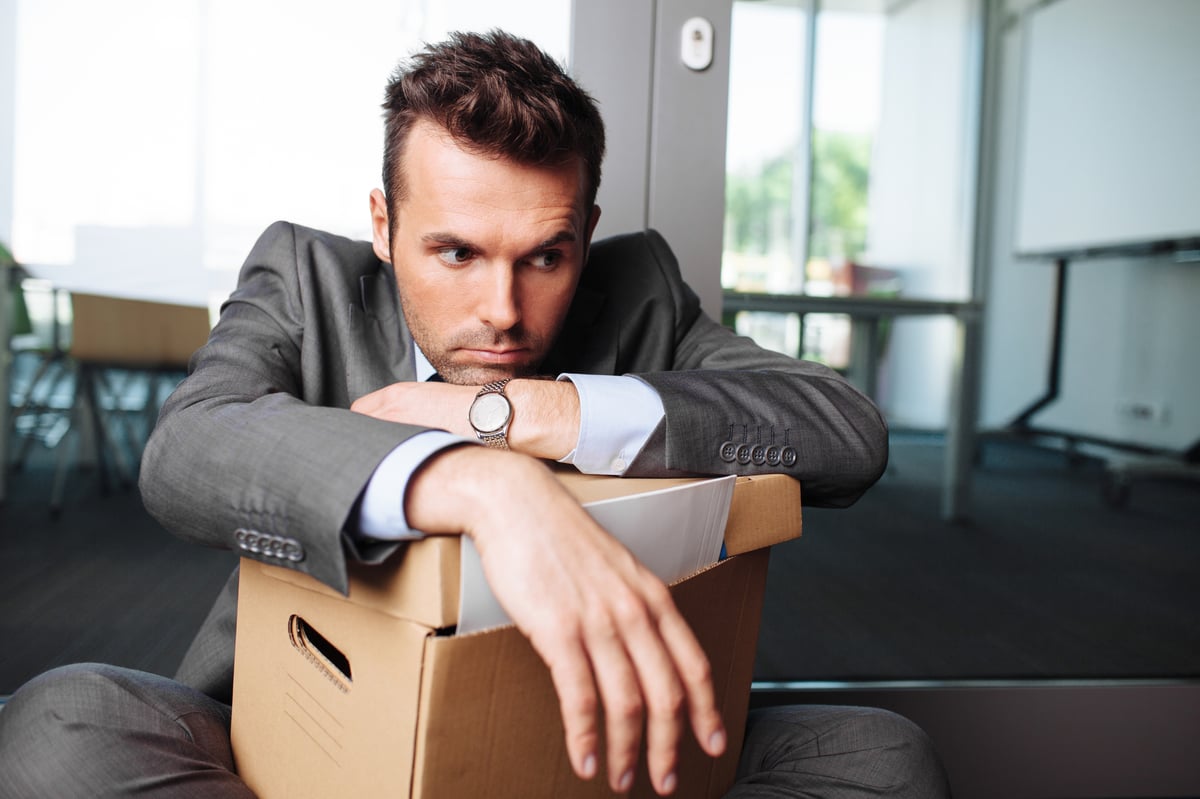 A sad man in a suit leaning on a box with his office supplies in it