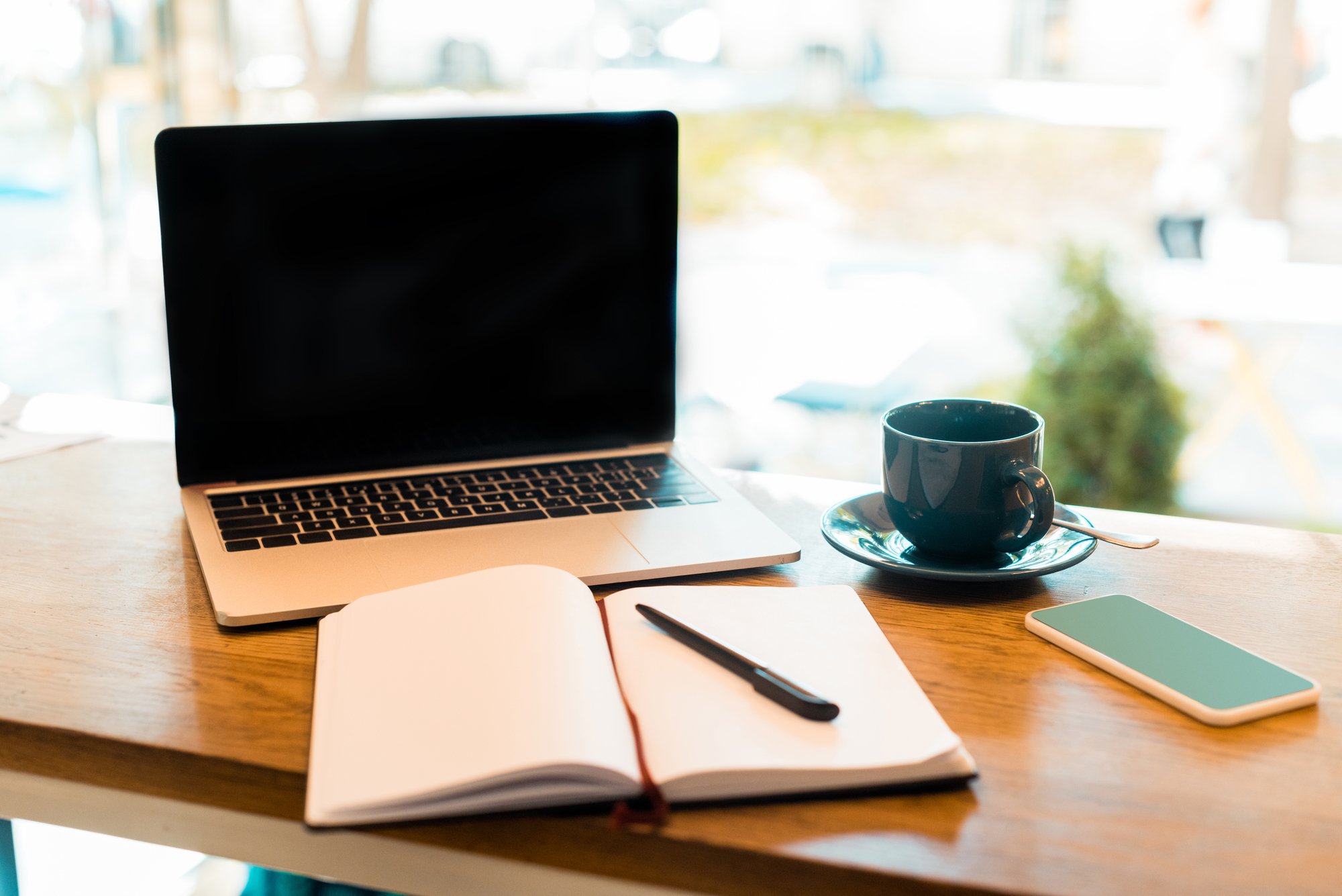 Laptop with blank screen, notebook and cup of tea on wooden cafe counter-1