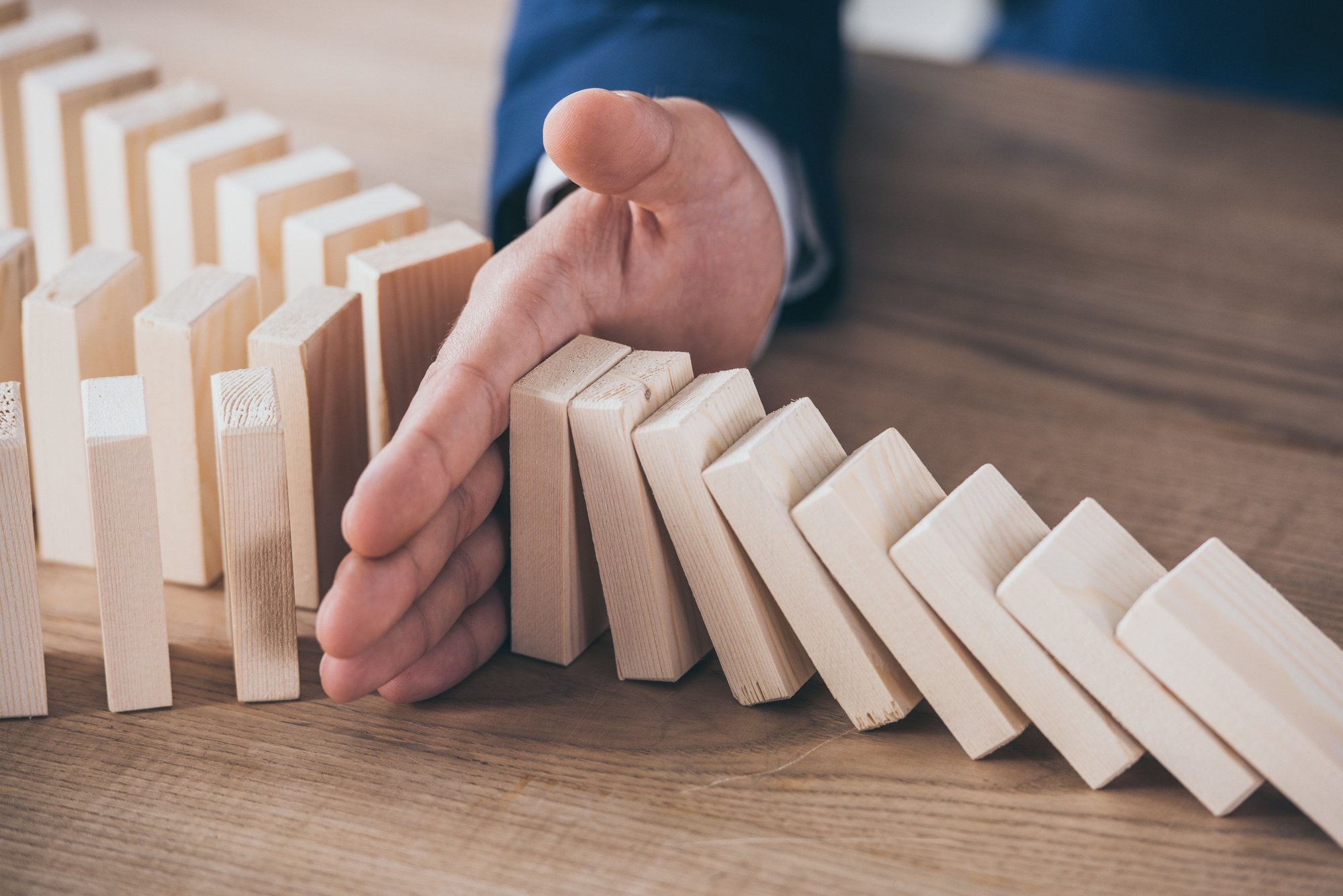 Partial view of risk manager blocking domino effect of falling wooden blocks