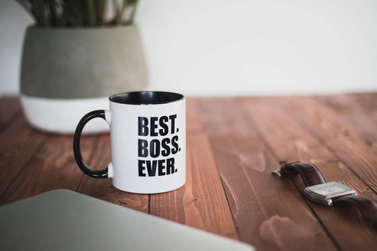 A coffee mug with best boss ever written on it on a wooden desk office with plant, laptop and watch