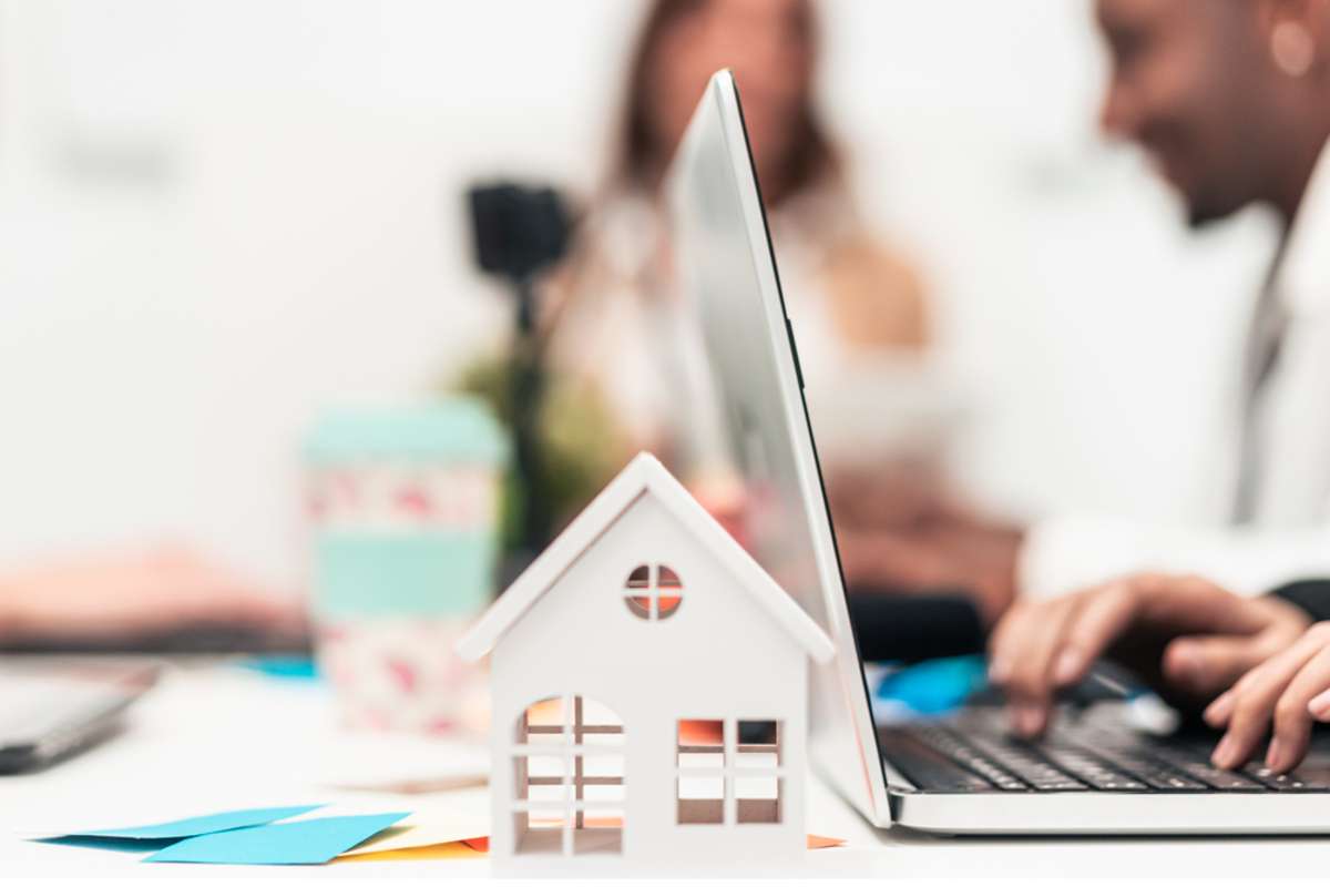 A laptop next to a small house model. Using a content marketing agency can help drive more property management leads