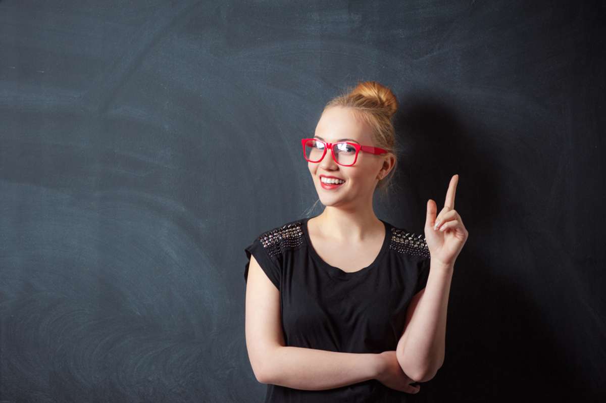 Attractive young blond woman pointing up against blackboard