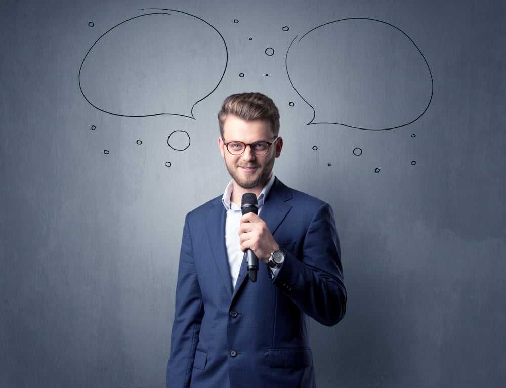 Businessman speaking into microphone with speech bubbles over his head