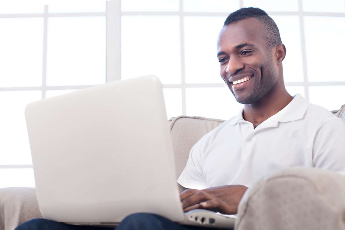 Cheerful African man using computer and smiling while sitting on the chair