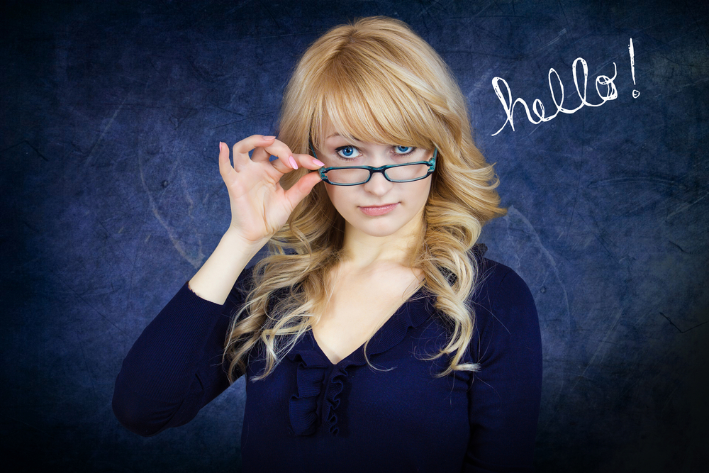 Closeup portrait young attractive woman with blue glasses peering above frames, flirting with you, isolated blue-gray background. Positive emotion facial expression feelings, attitude, body language