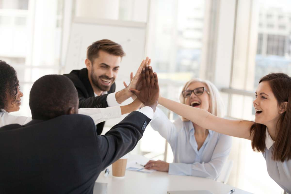 Excited multiracial office associates employees group giving high five engaged in coaching team spirit