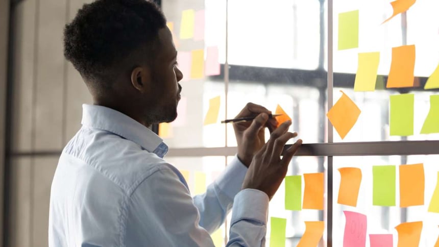 Focused African American male employee write on colorful sticky notes develop business project in office