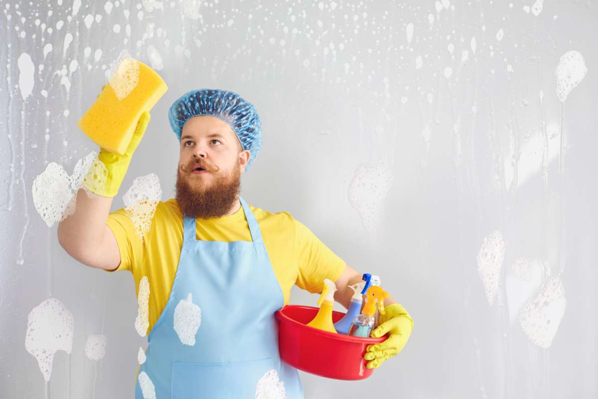Funny fat man with a beard in an apron washing cleans up on a gray background