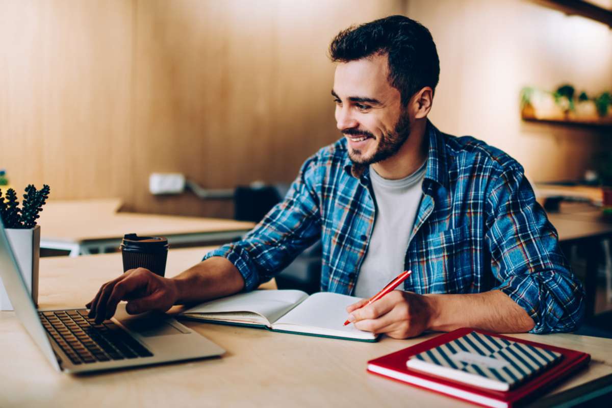 Happy man reading a laptop screen and taking notes, property management websites concept