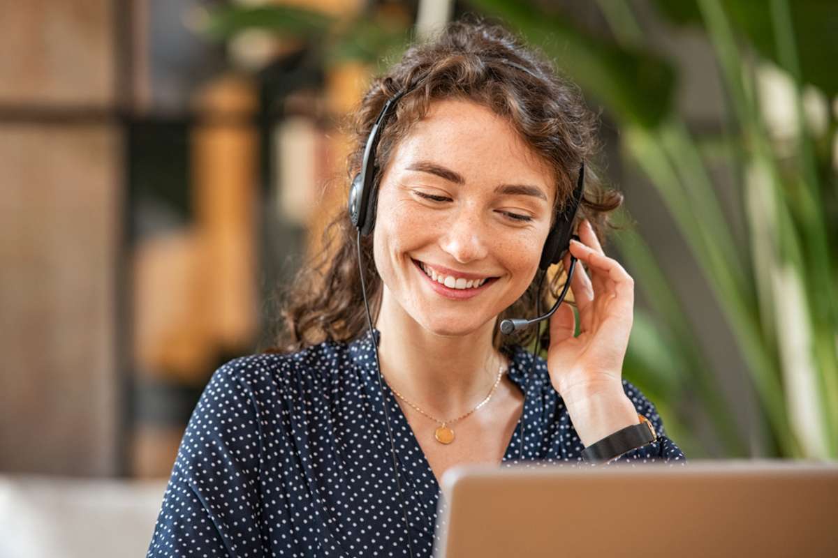Happy young woman working on laptop while talking to customer on phone