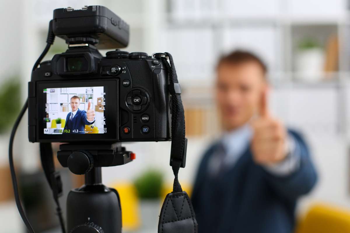 Male in suit and tie show confirm sign arm making promo videoblog or photo session in office camcorder to tripod closeup