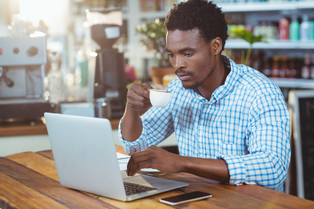 Man using a laptop while having cup of coffee in cafe