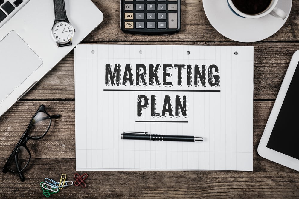 Marketing Plan written on note pad, office desk with electronic devices