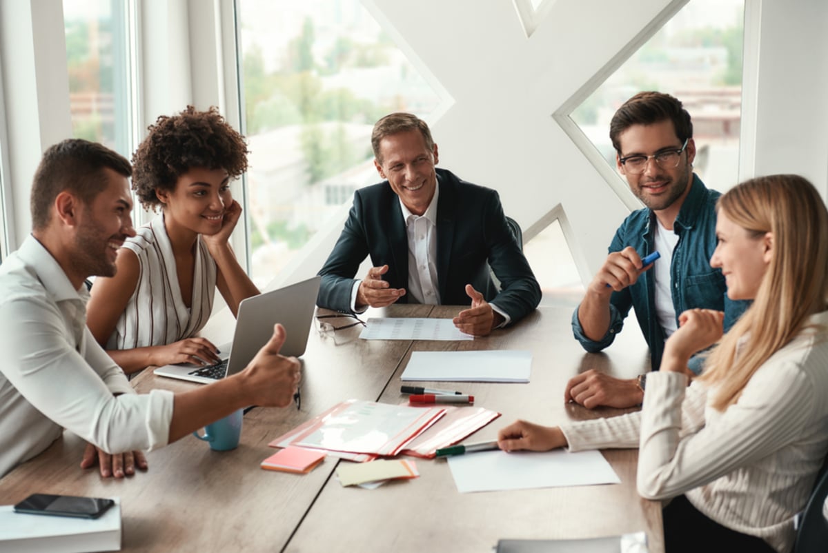 Multicultural team discussing something and smiling while sitting at the office table