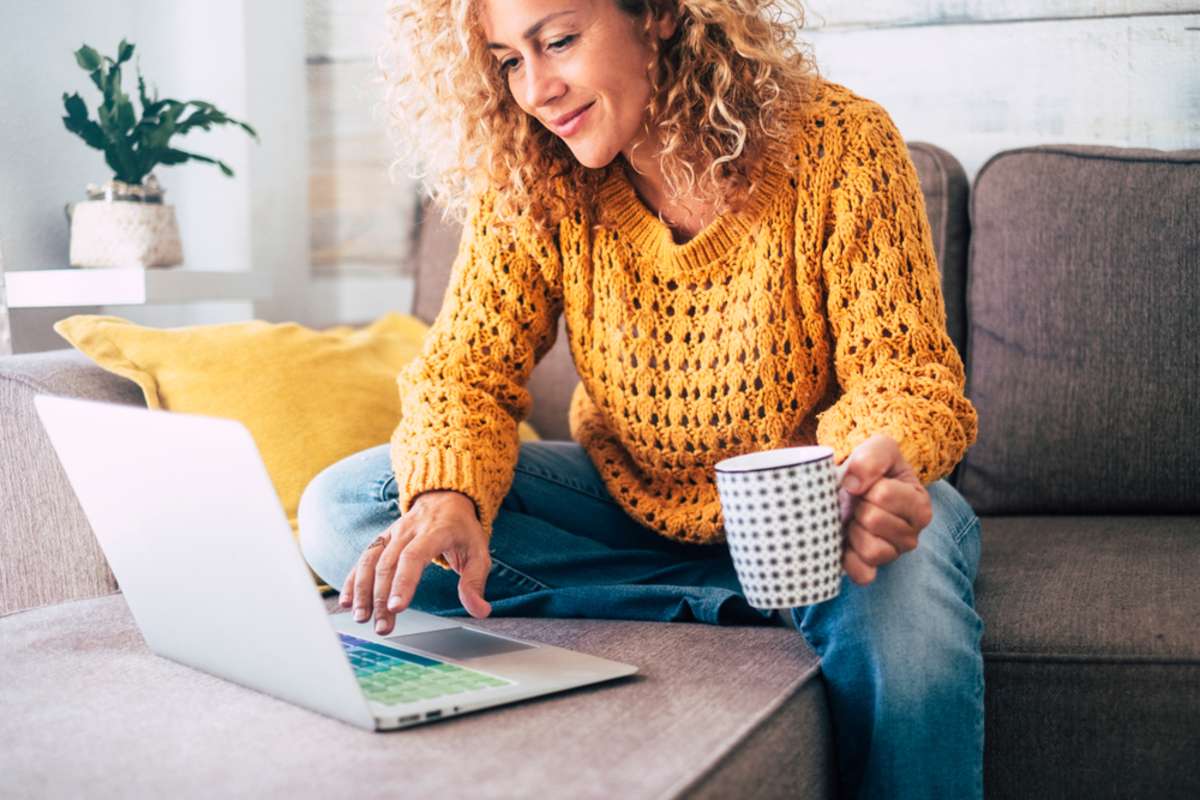 Nice beautiful lady with blonde curly hair work at the notebook sit down on the sofa at home