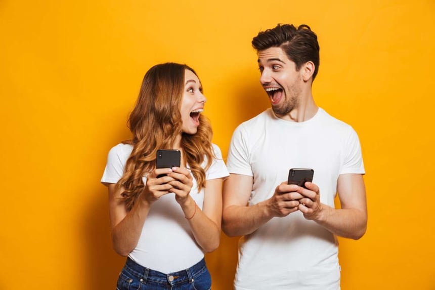Photo of positive excited people man and woman screaming and looking at each other while both using mobile phones isolated over yellow background-1