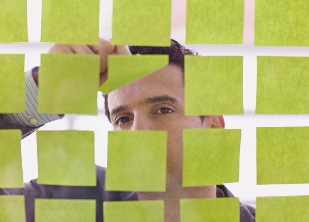 Portrait of a middle eastern business man behind sticky notes in bright glass office