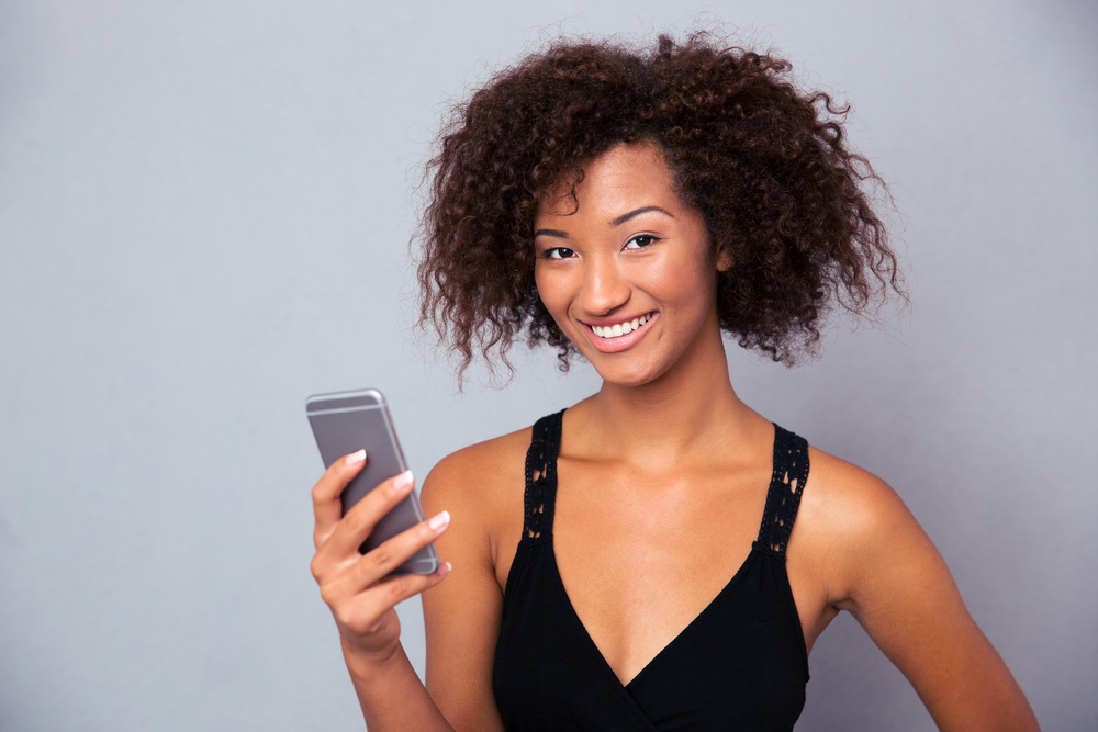 Portrait of a smiling afro american woman using smartphone over gray background