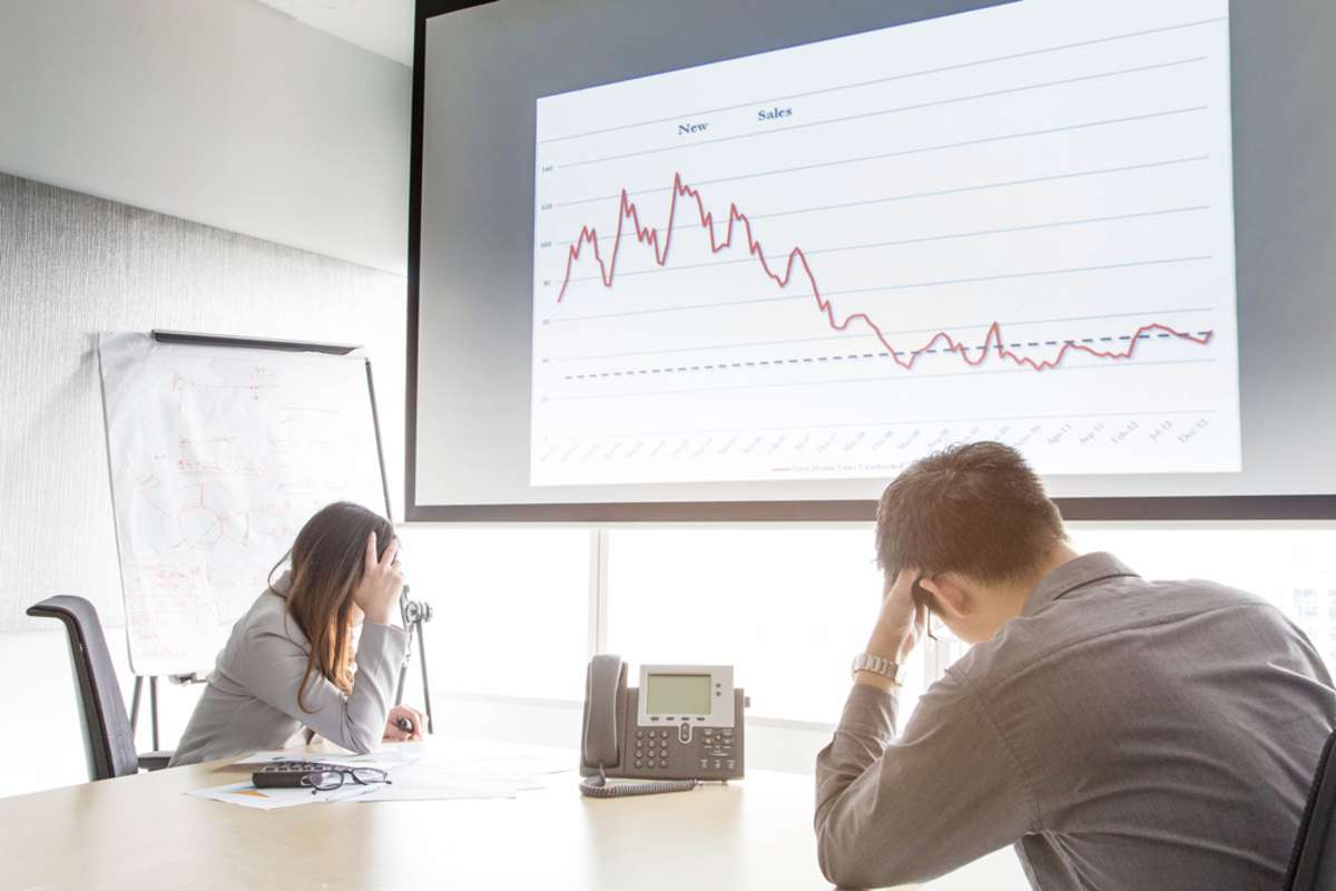 Serious and fail business man and woman in meeting room with negative graph on screen