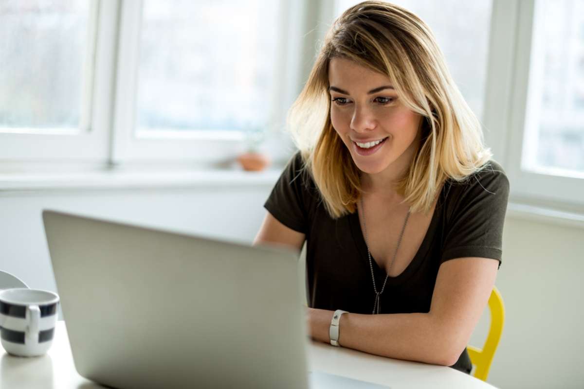 Smiling woman looks at a laptop and learns from a pillar page. 