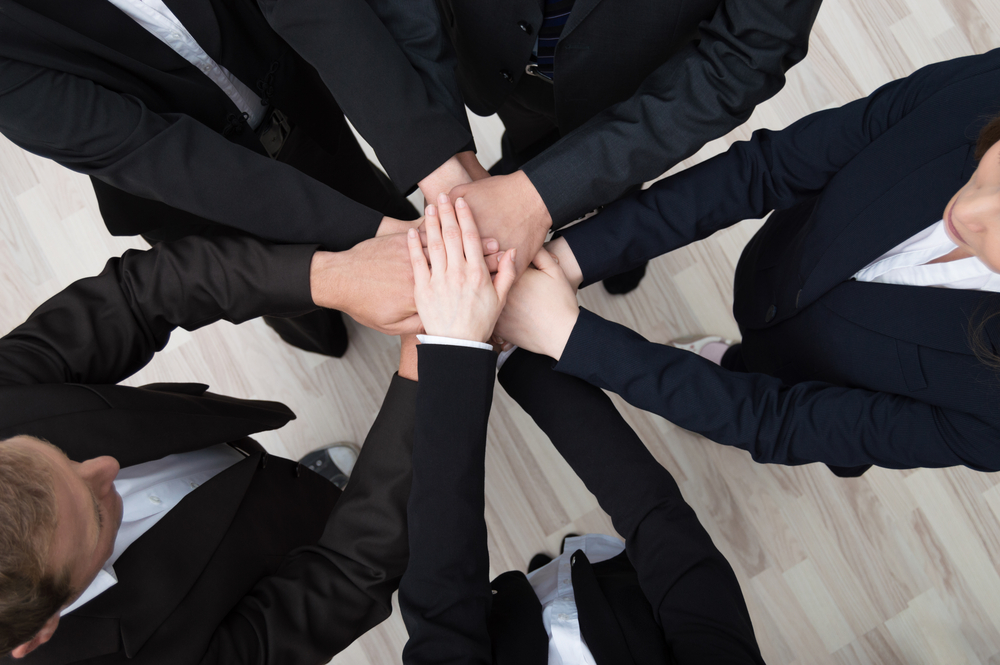 Teamwork - conceptual image of a group of young professional businesspeople standing in a circle facing each other clasping hands