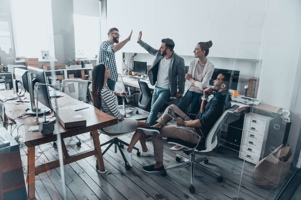 Two cheerful young business people giving high-five while their colleagues looking at them and smiling