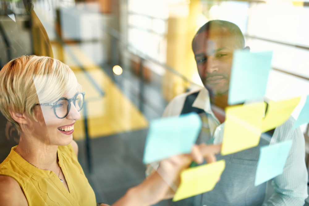 Two professionals brainstorming using adhesive notes in window, property management marketing strategy concept. 