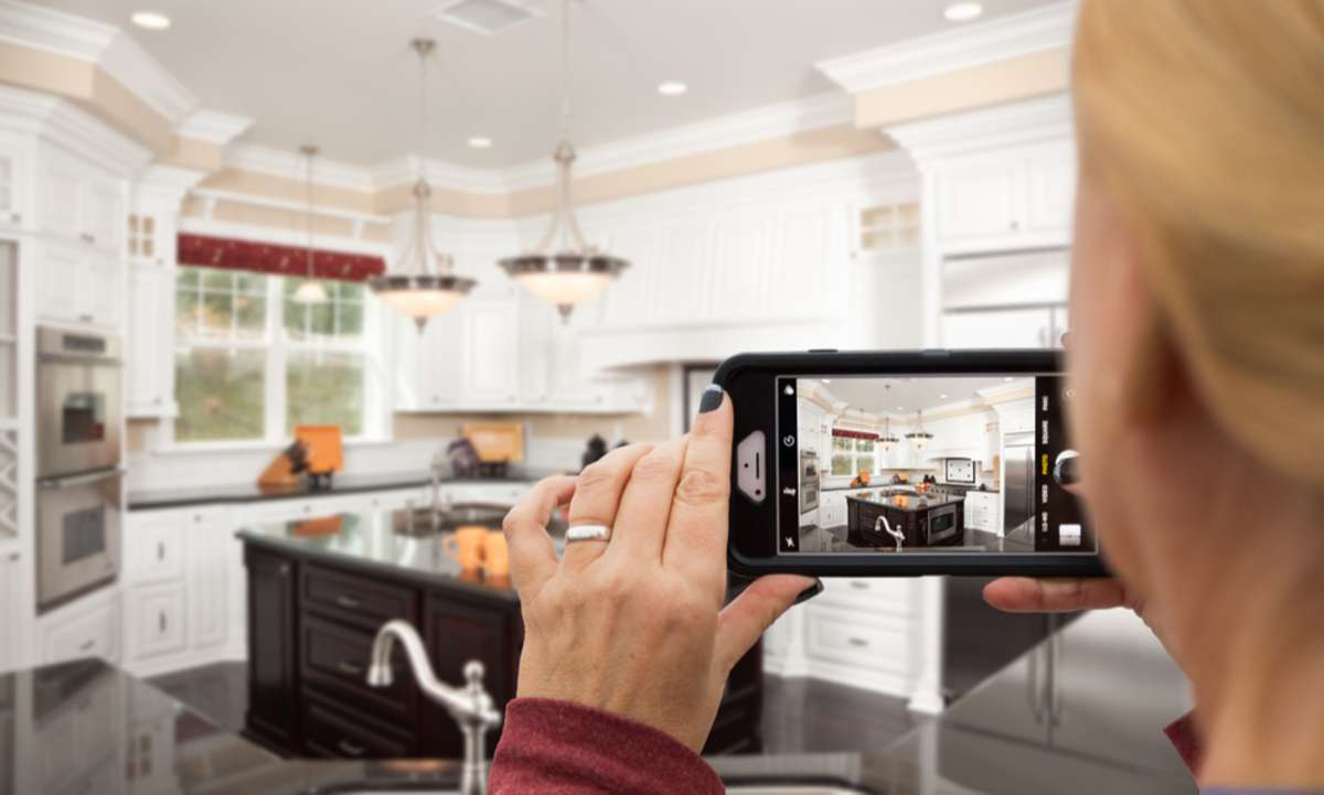 Woman taking pictures of a kitchen with her smart phone as a form of visual marketing. 