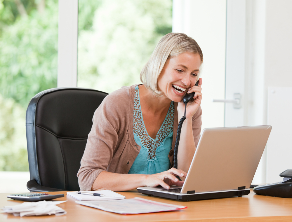 Woman working on her computer while she is phoning at home