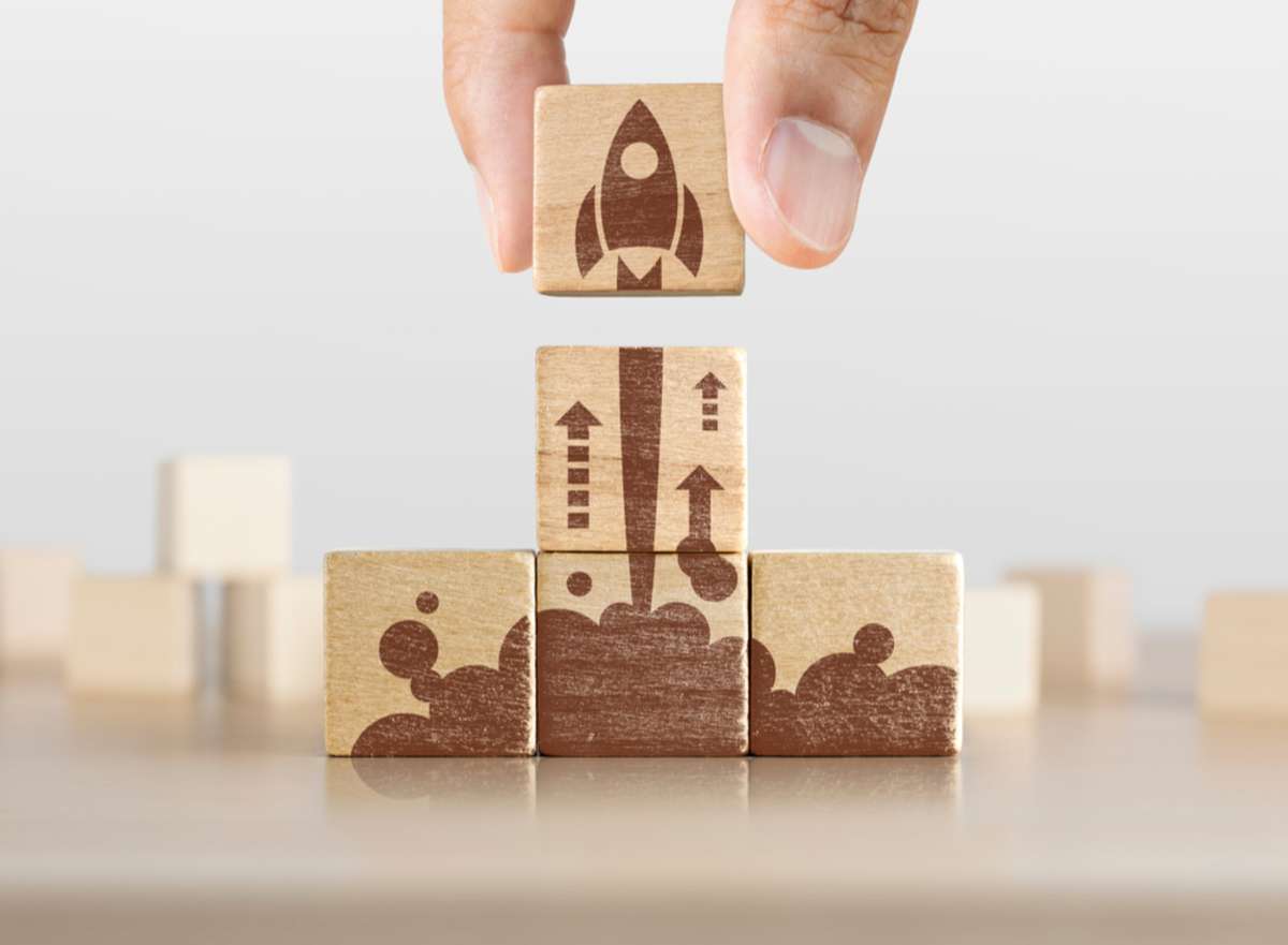 Wooden blocks with launching rocket graphic arranged in pyramid shape and a man is holding the top one