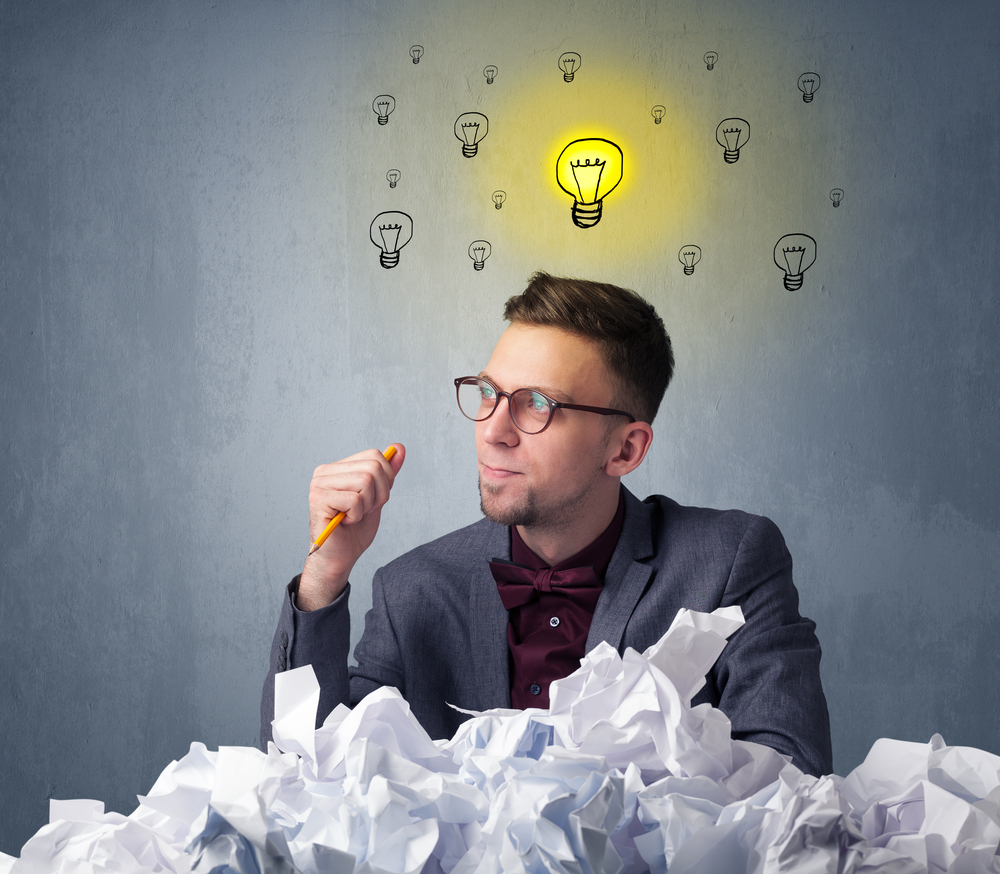 Young businessman sitting behind crumpled paper with lightbulbs above his head