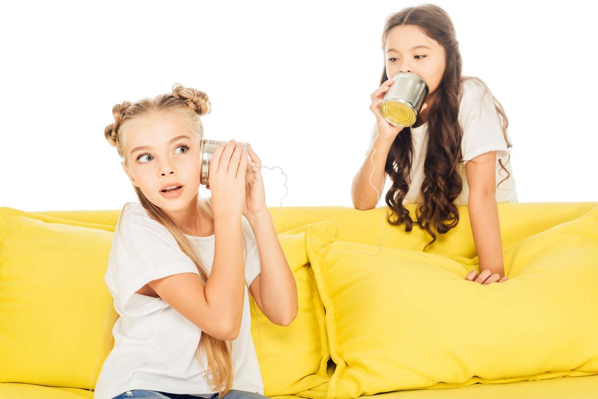 excited kids playing with tin cans phone on yellow sofa isolated on white