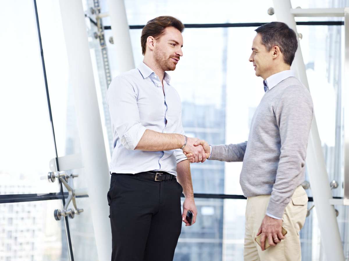 two caucasian business executives in casual wear shaking hands in office