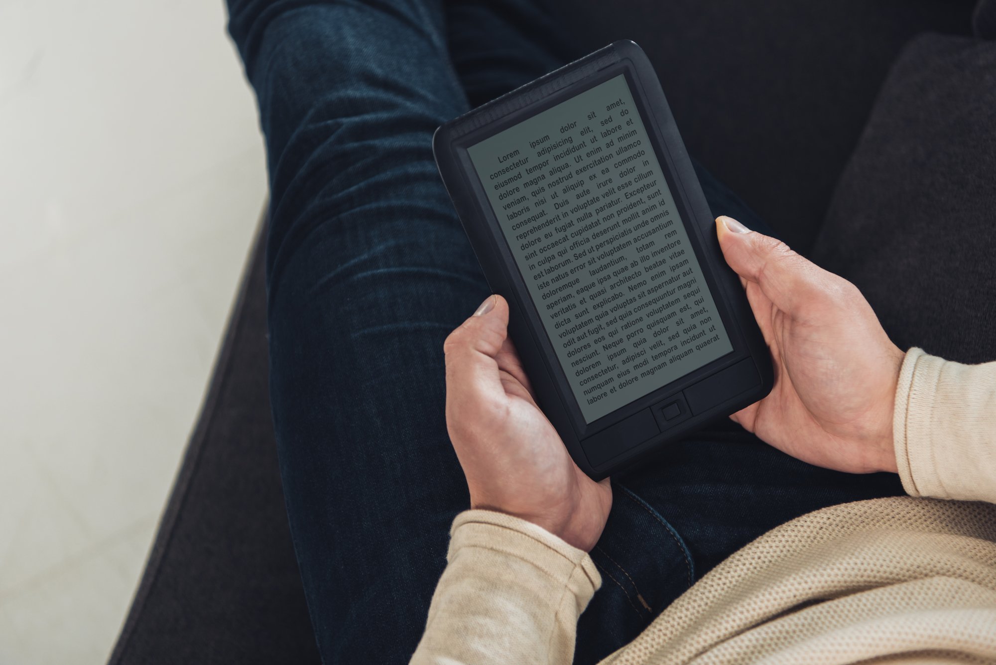Top view of ebook in hands of man sitting on sofa