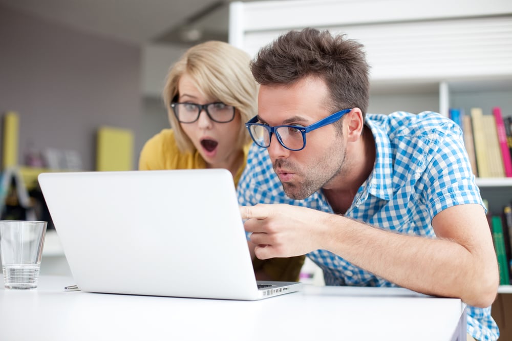 Two people looking confused at laptop screen, SEO content challenges concept. 