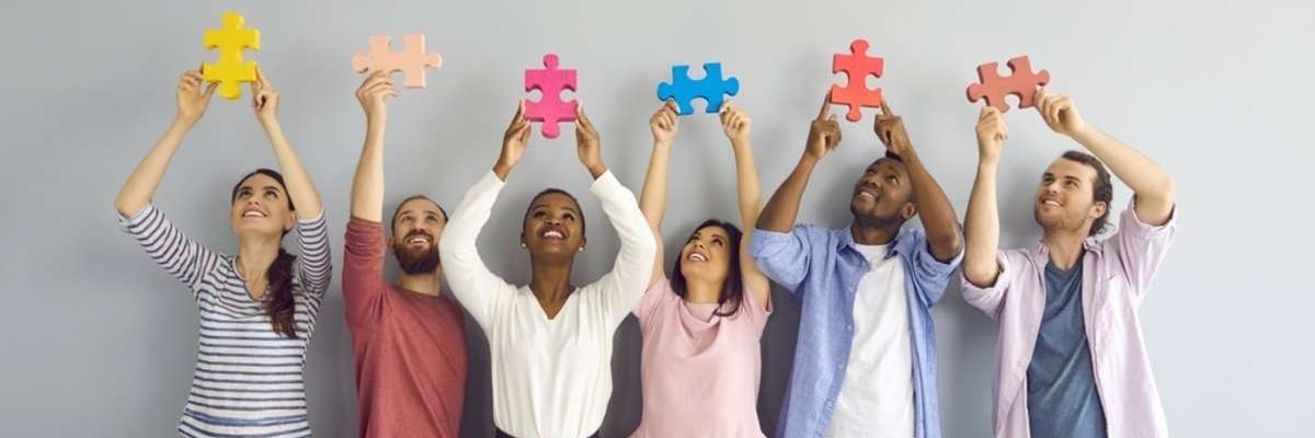 Group of happy smiling multiracial young people holding colorful puzzle pieces over their heads