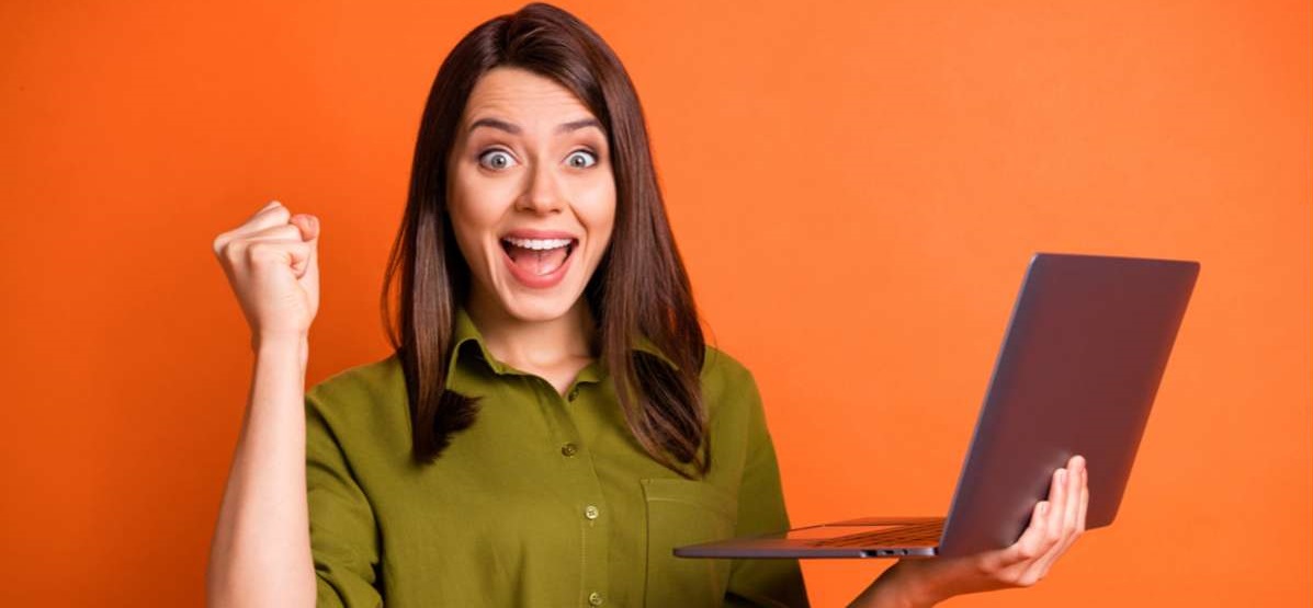 Photo portrait of amazed brunette using laptop gesturing like winner isolated on vibrant orange color background